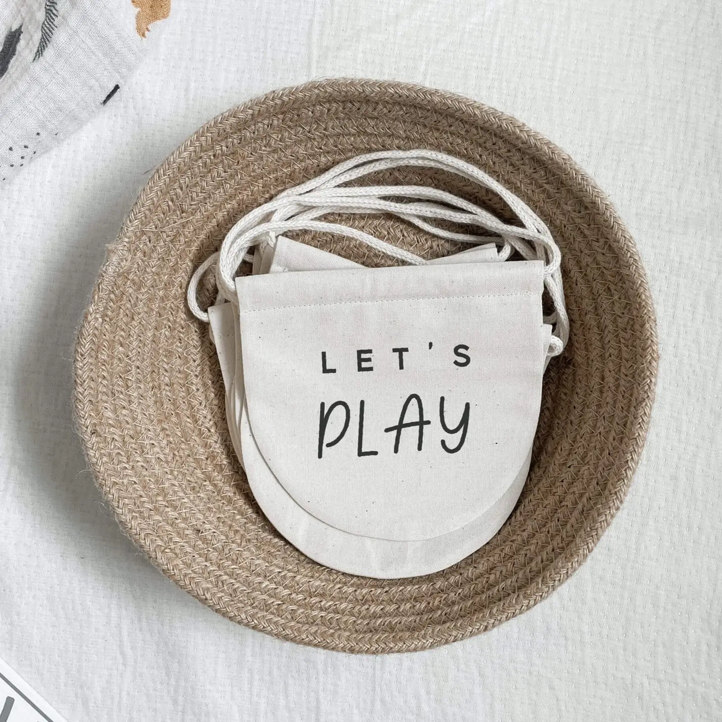 Pile of beige banners with 'Let's Play' printed on them, stacked in a pale brown woven basket