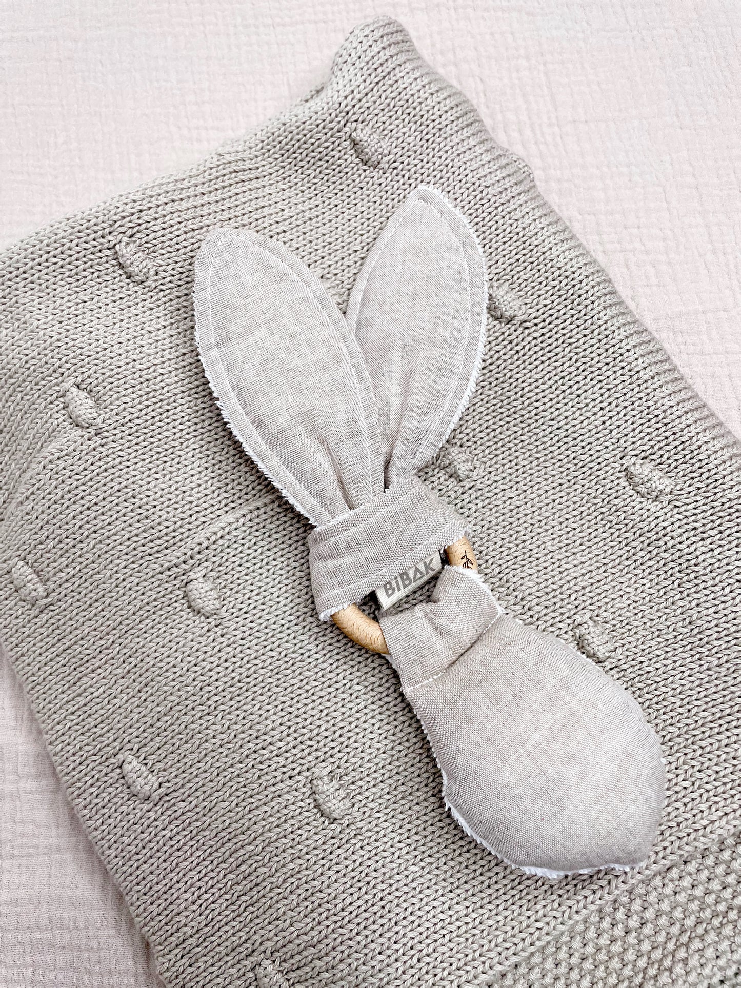 folded up knitted blanket in stone, with a rabbit teether on top of it