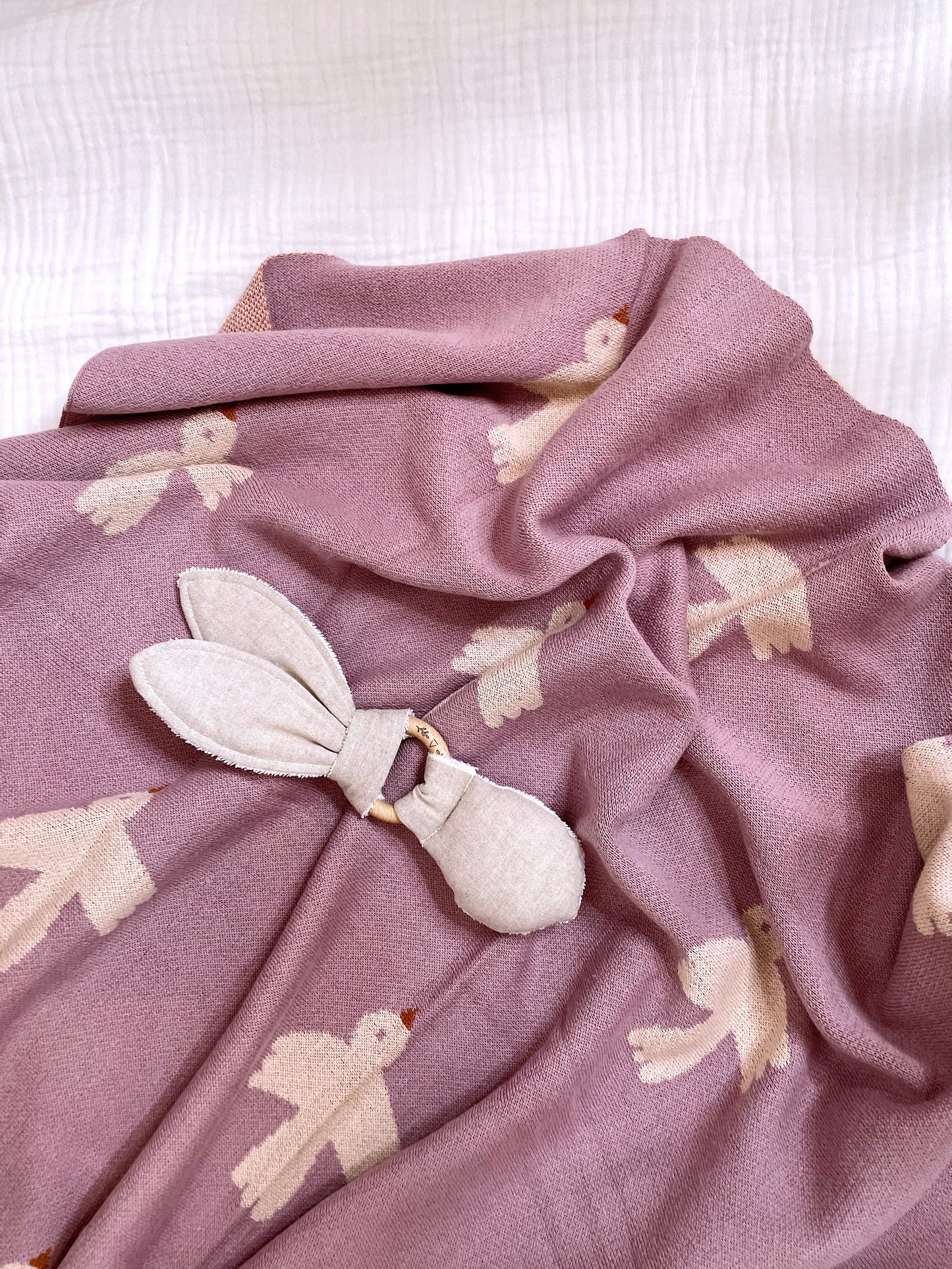 purple blanket with birds on it, with a greige rabbit rattle teether on top