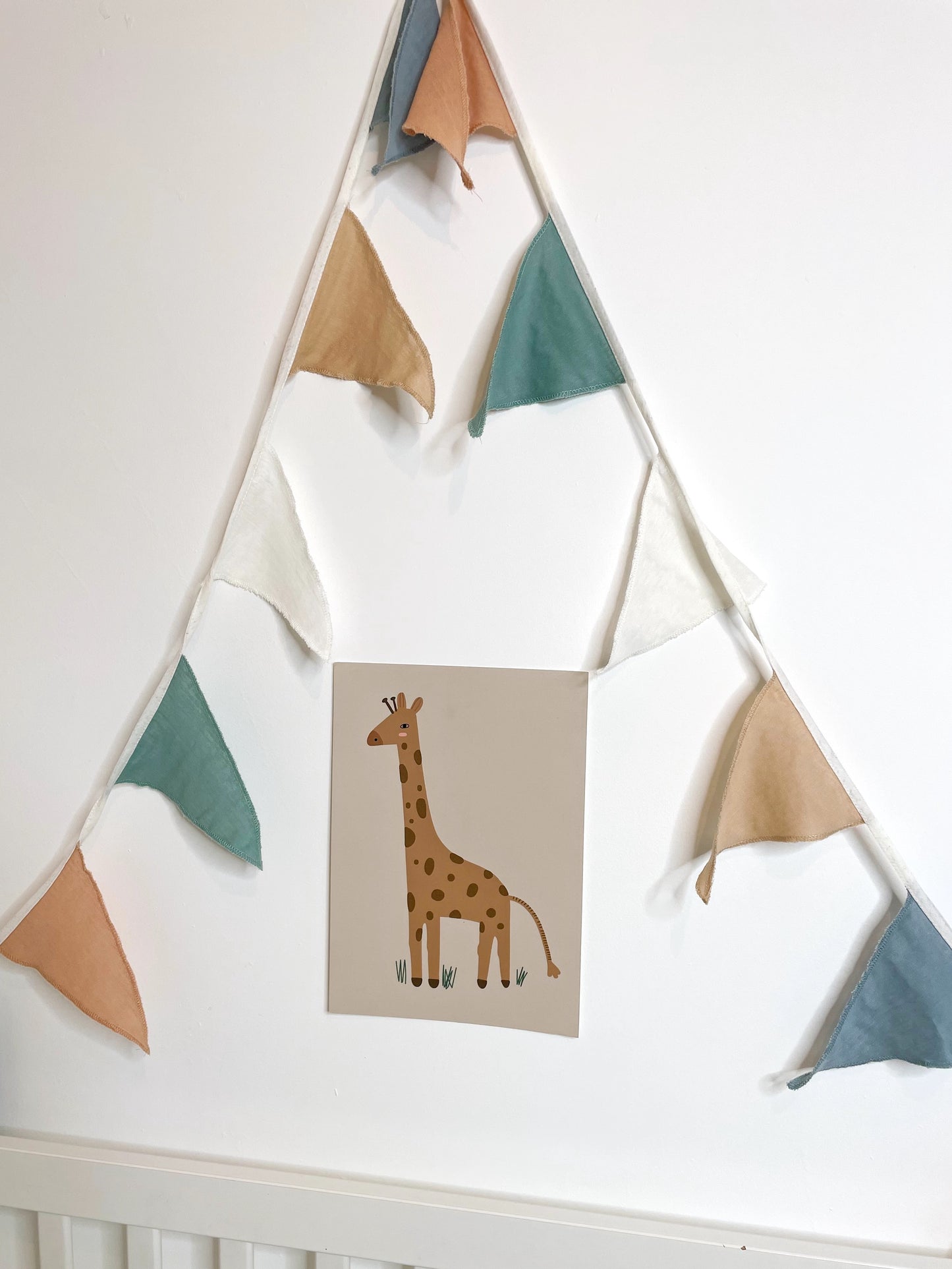 pastel muslin bunting hung around a print of a giraffe, on a white wall