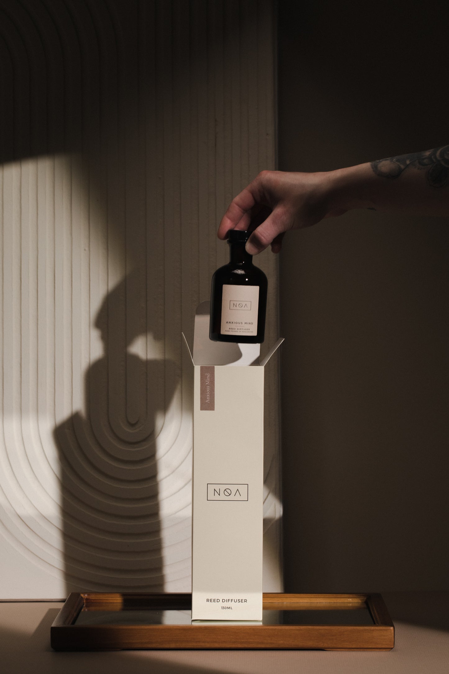 a black glass reed diffuser bottle being picked out of a tall white cardboard box