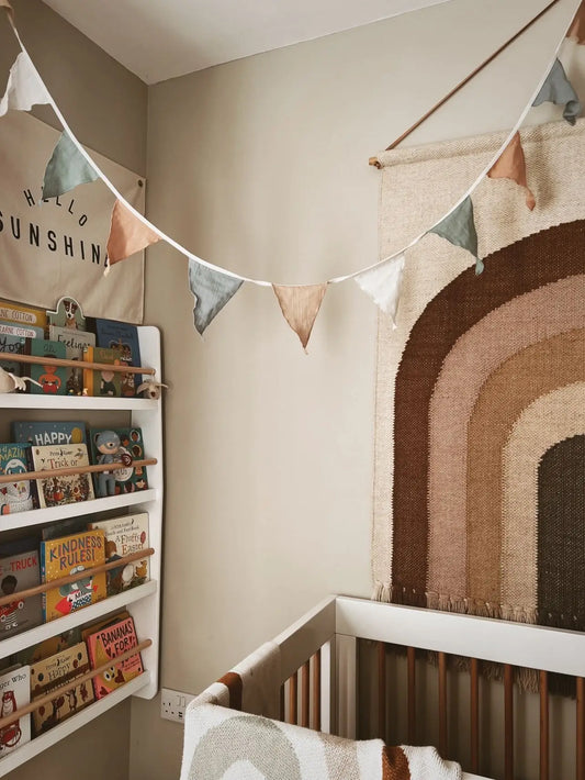 child's bedroom with cot, wall hanging, book shelves and pastel bunting hanging across the forefront of the image