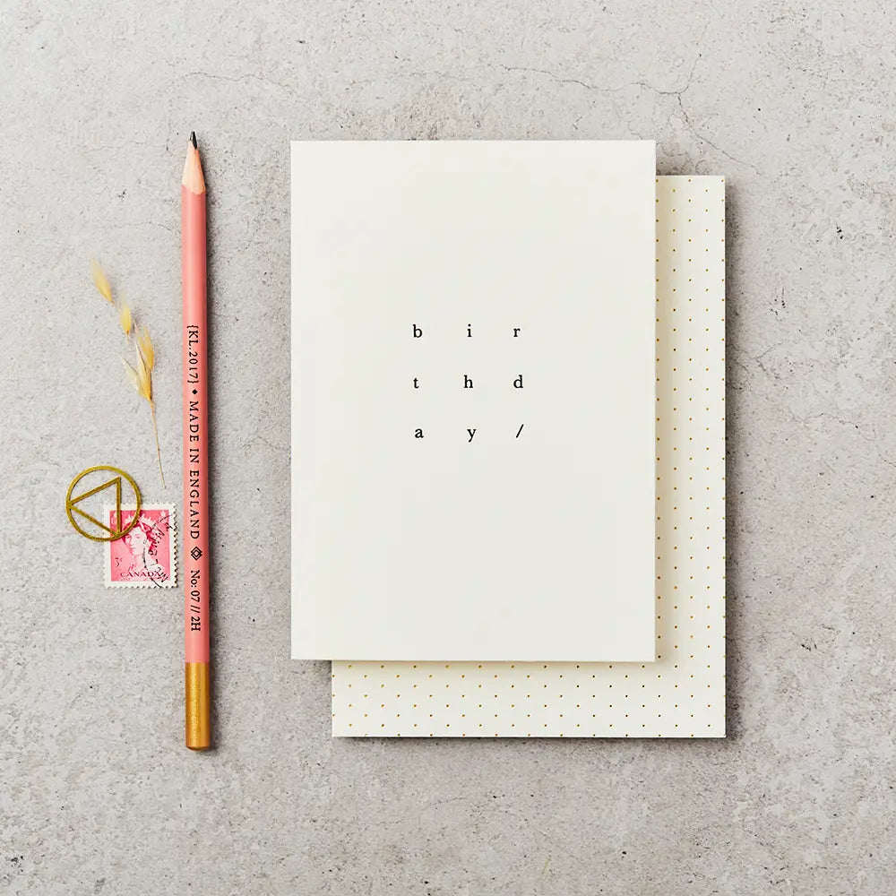 cream greeting card with birthday written on it in simple black type, next to a pencil and stamp