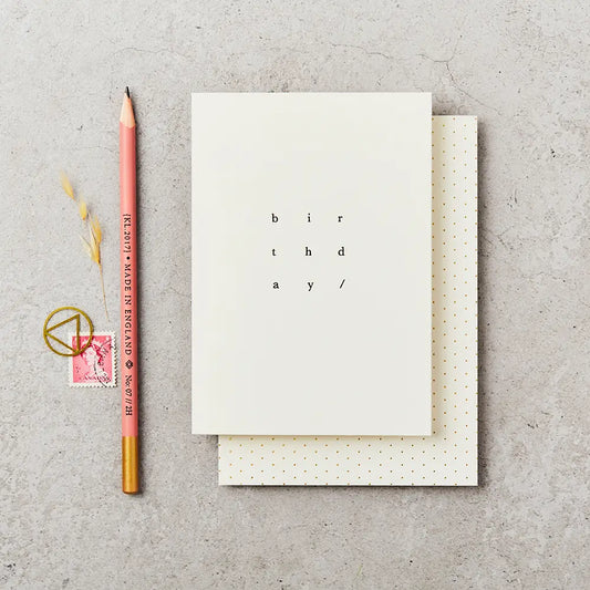 cream greeting card with birthday written on it in simple black type, next to a  pencil and stamp