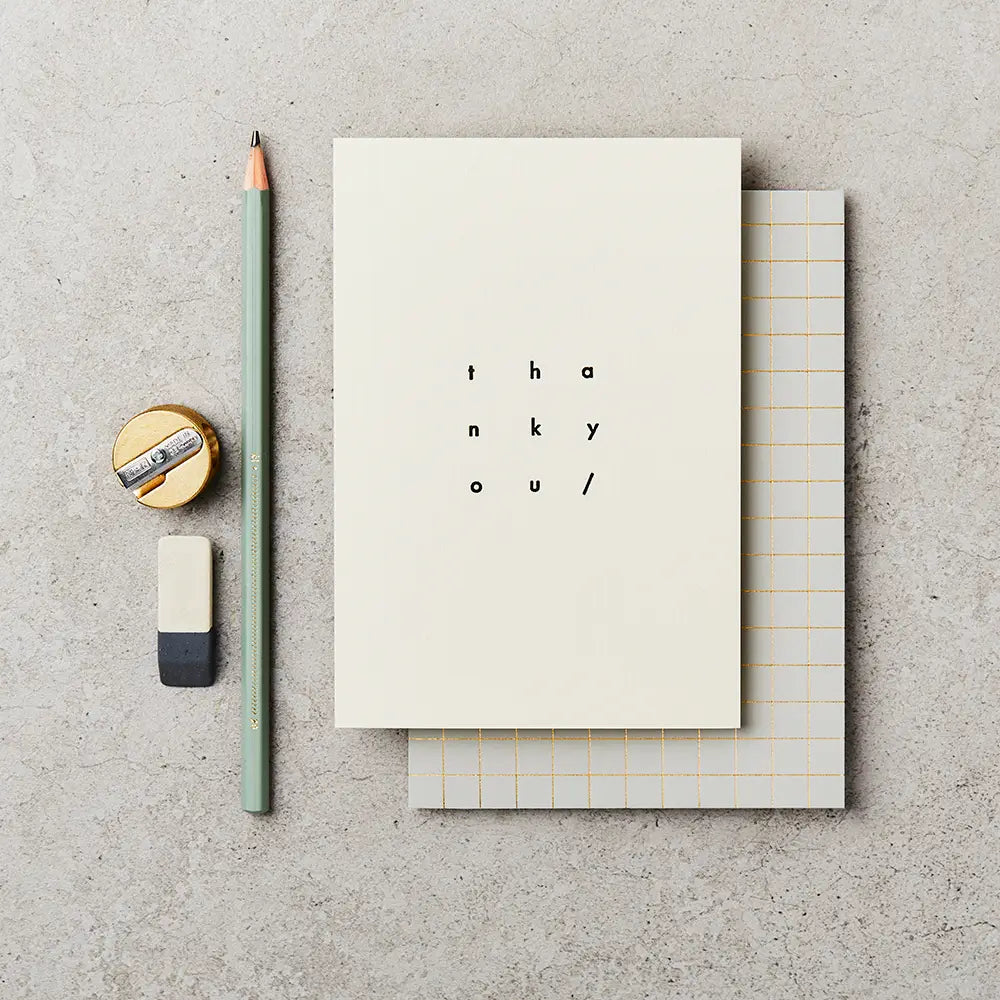 cream greeting card with thank you on the front in a black ink and square design, laid next to a pencil, sharpener and rubber
