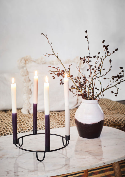 monochrome vase with sticks with berries on inside, next to a black round candle holder with space for four candles, three candles are monochrome and one is white, all set on a marble table