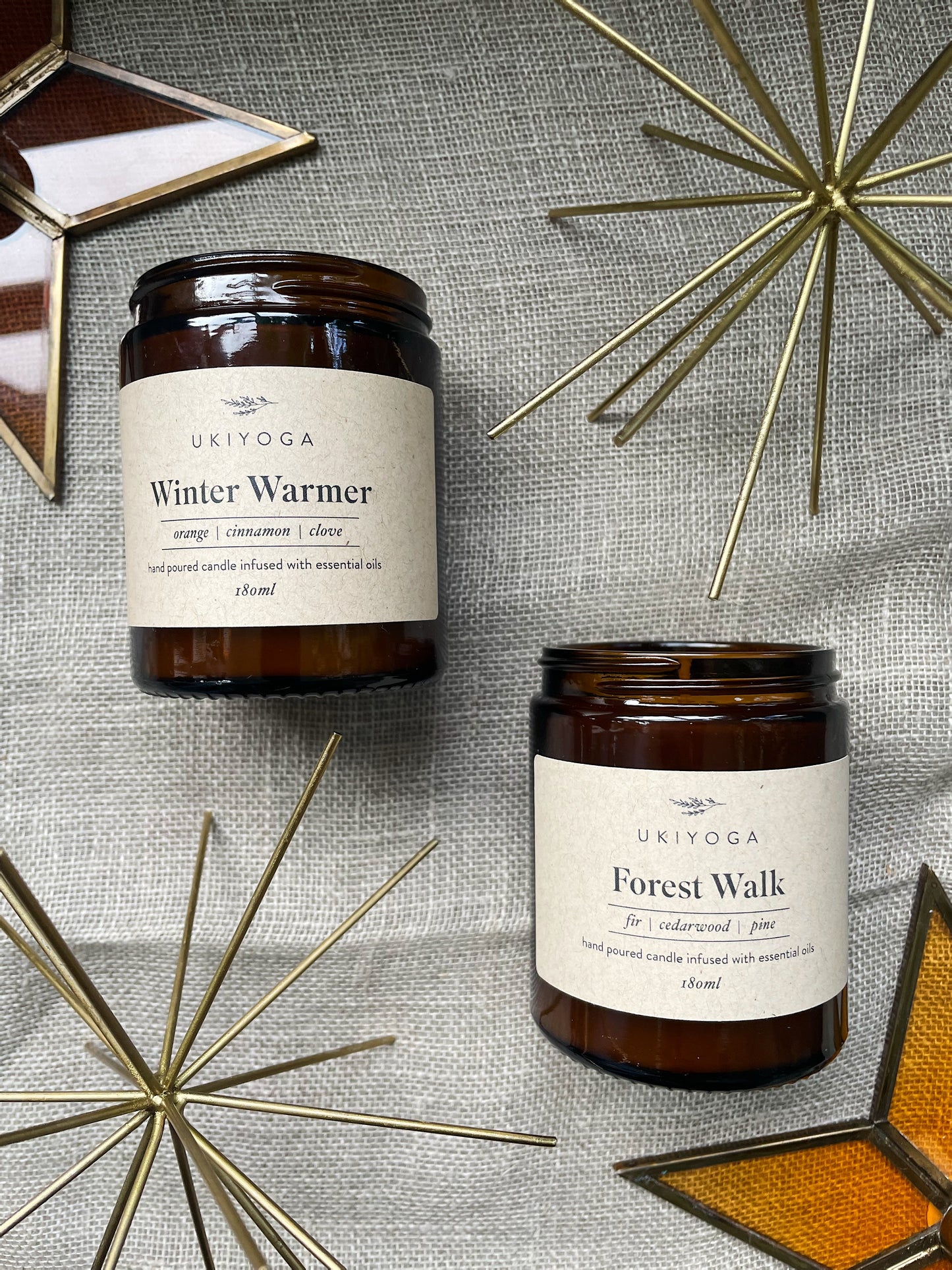 Two candles in amber glass jars on a beige background, next to a brass twinkle and colourful glass stars