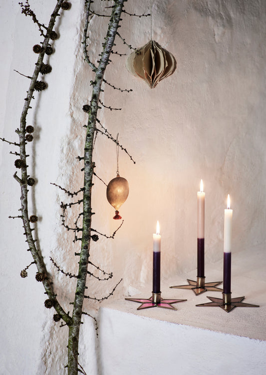 three candles in glass star candle holders, on a white ledge, next to a decorative branch with baubles