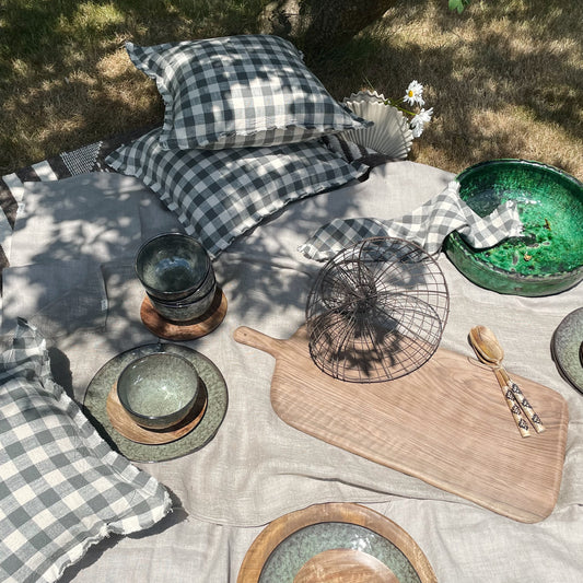 picnic set up with green plates and bowls mixed with wooden plates and boards, accessorised with check cushion covers and tea towels