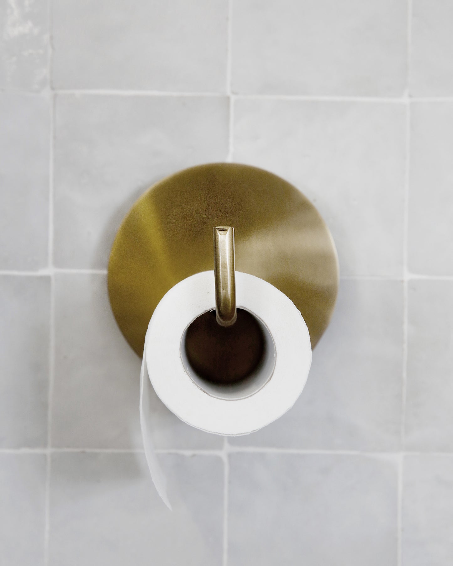 golden coloured iron toilet roll holder on a light grey tiled wall