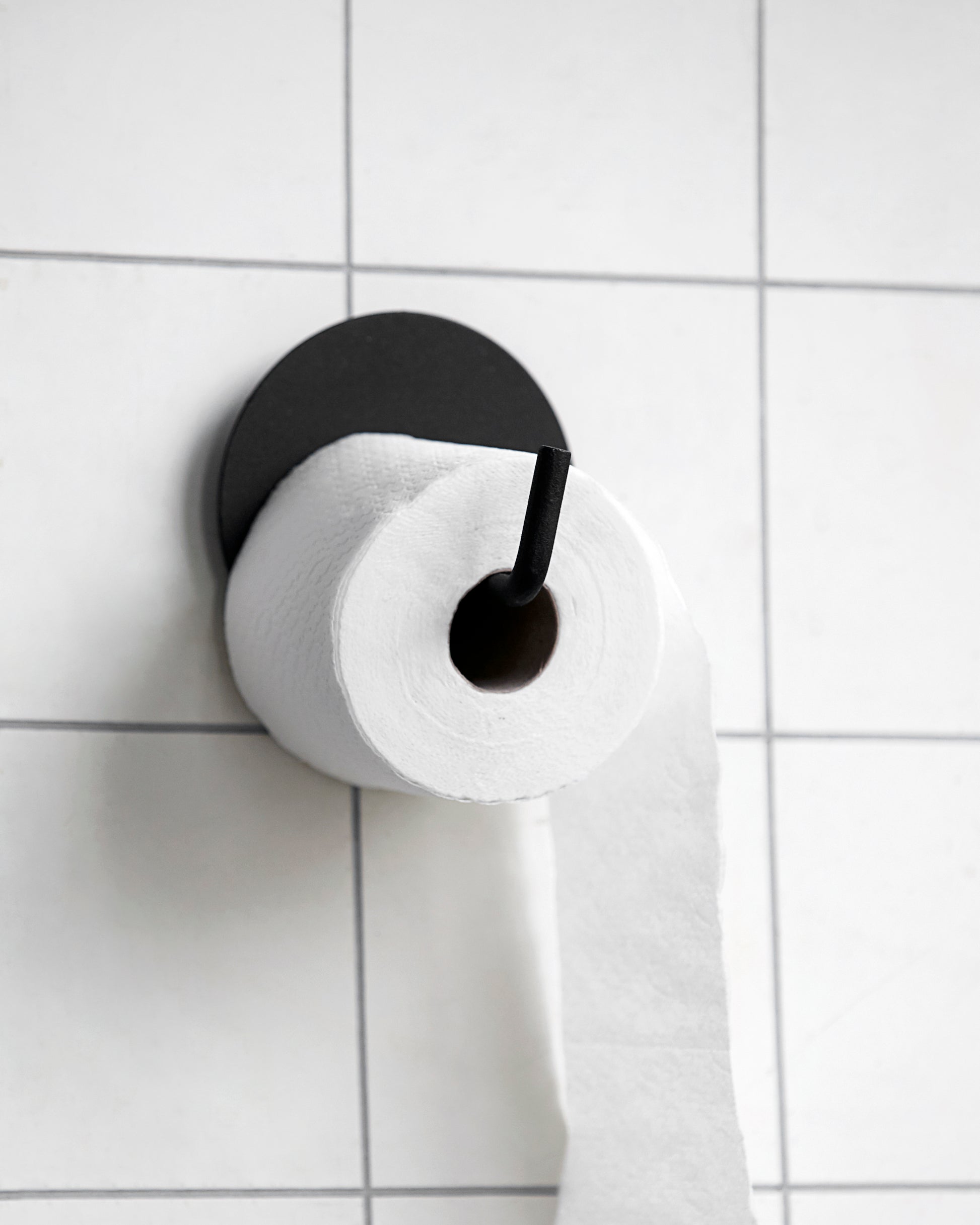 simple black toilet roll holder attached to a white tiled wall