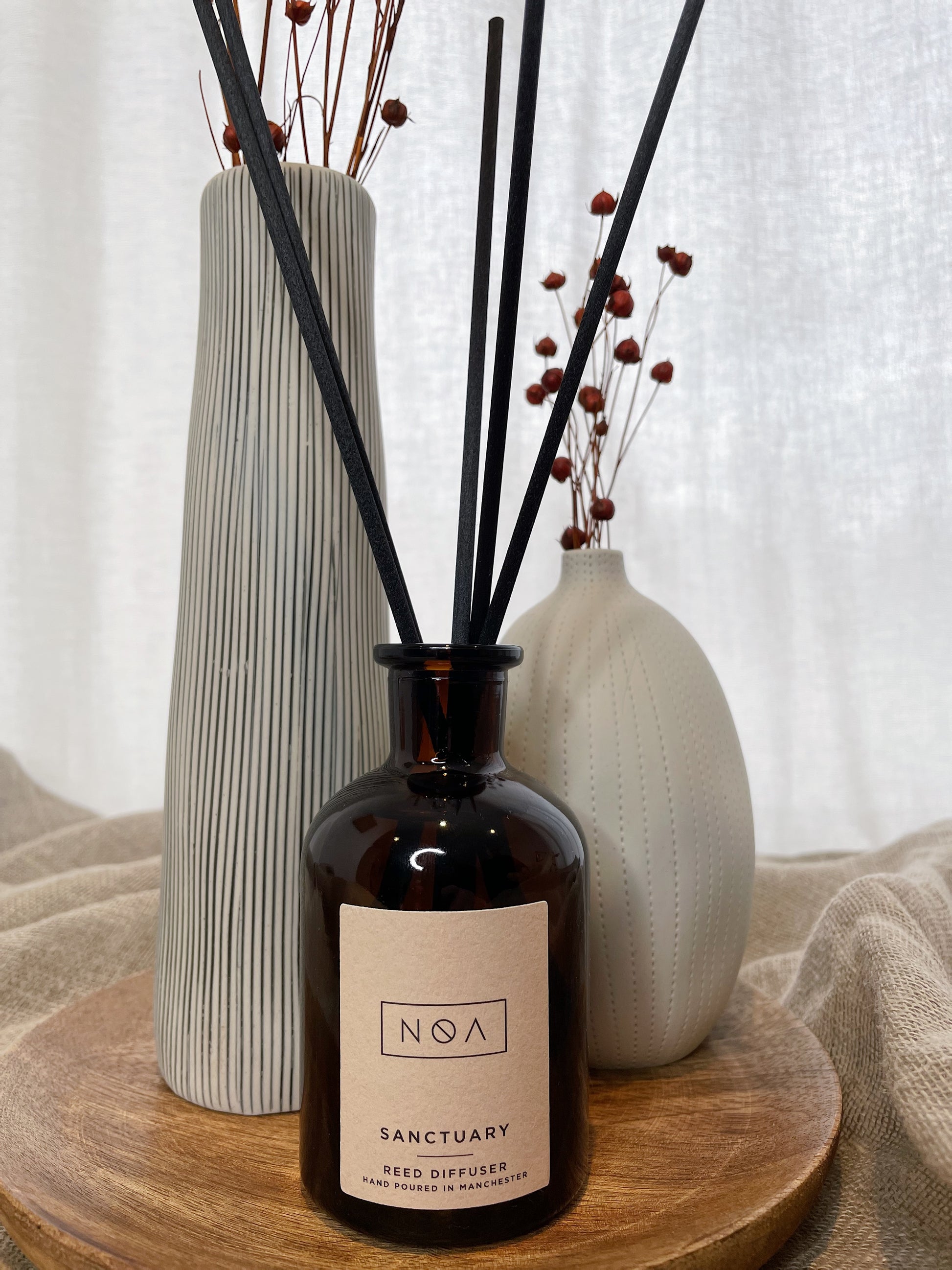 A brown glass diffuser, flanked by two vases - one black and white stripes, one white - on top of a wooden plate