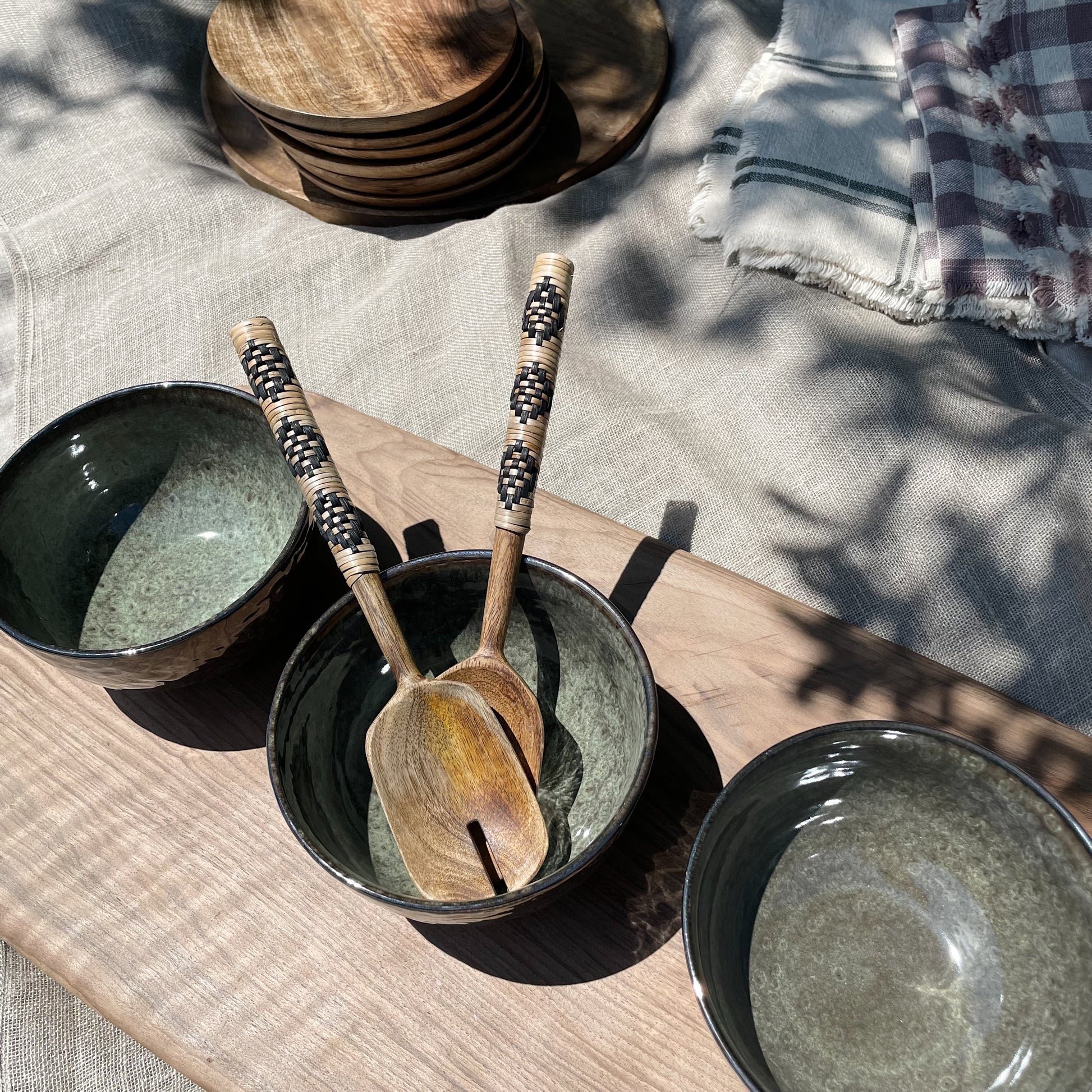 three dark green bowls on a wooden board, with wooden salad servers in the middle bowl