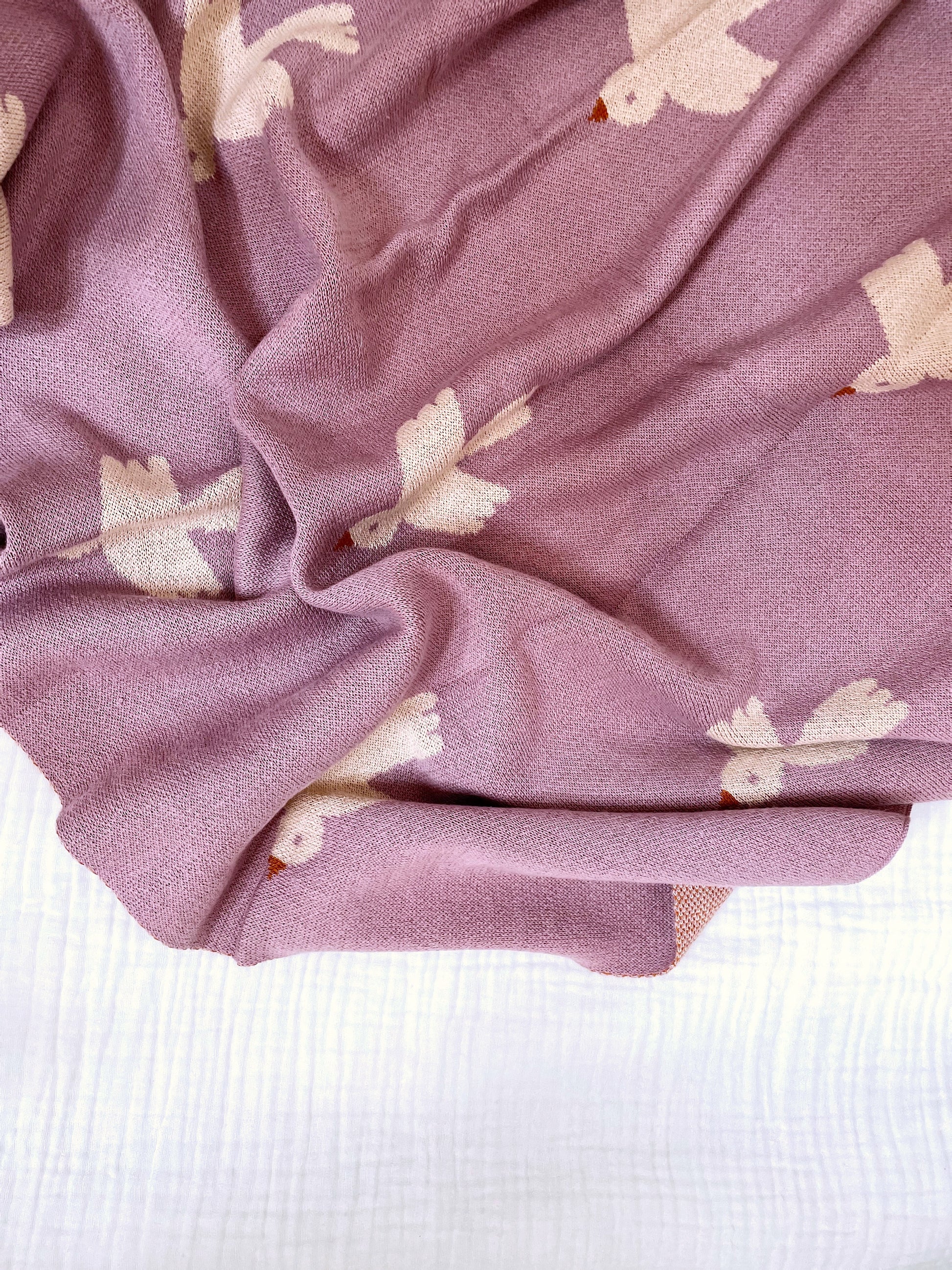 purple blanket with pale purple birds strewn on top of a pale beige blanket