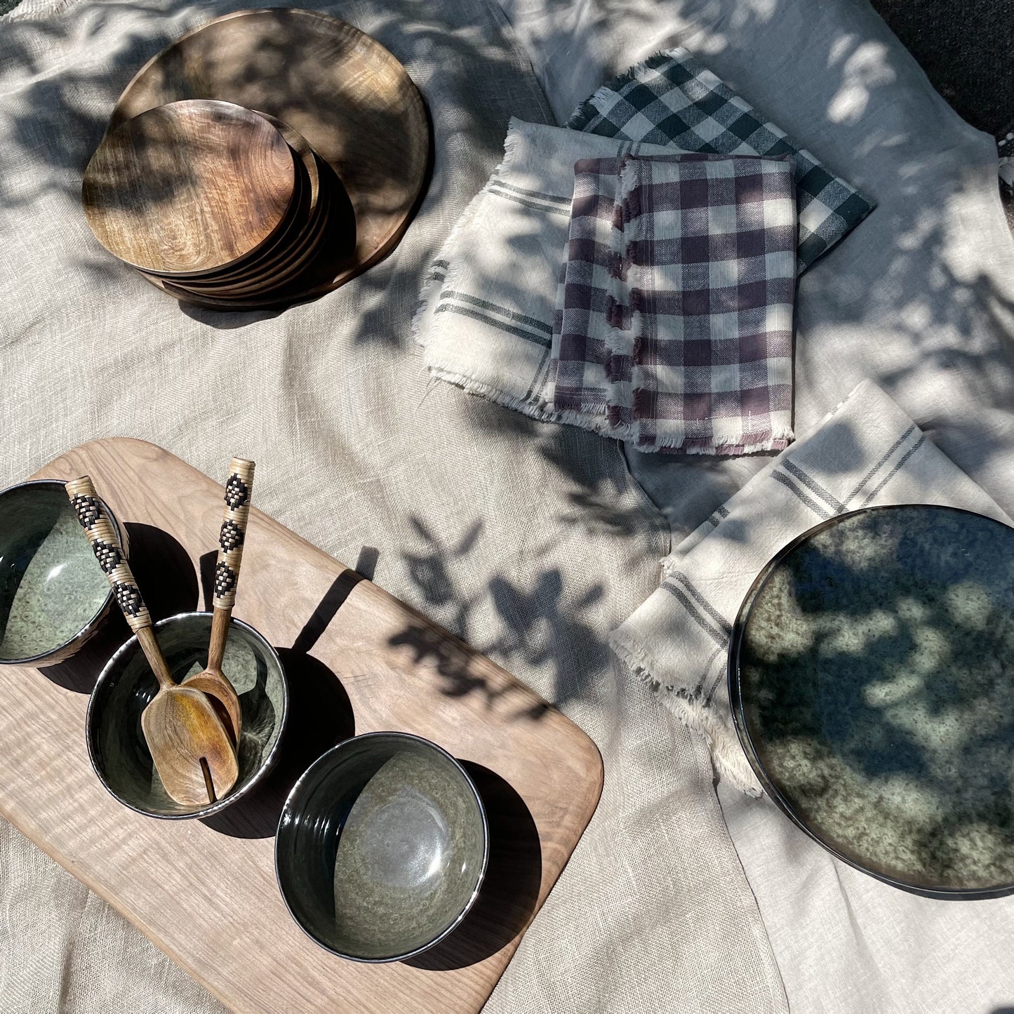picnic set up with dark green and black plate and bowls, along with wooden plates and boards and checked tea towels