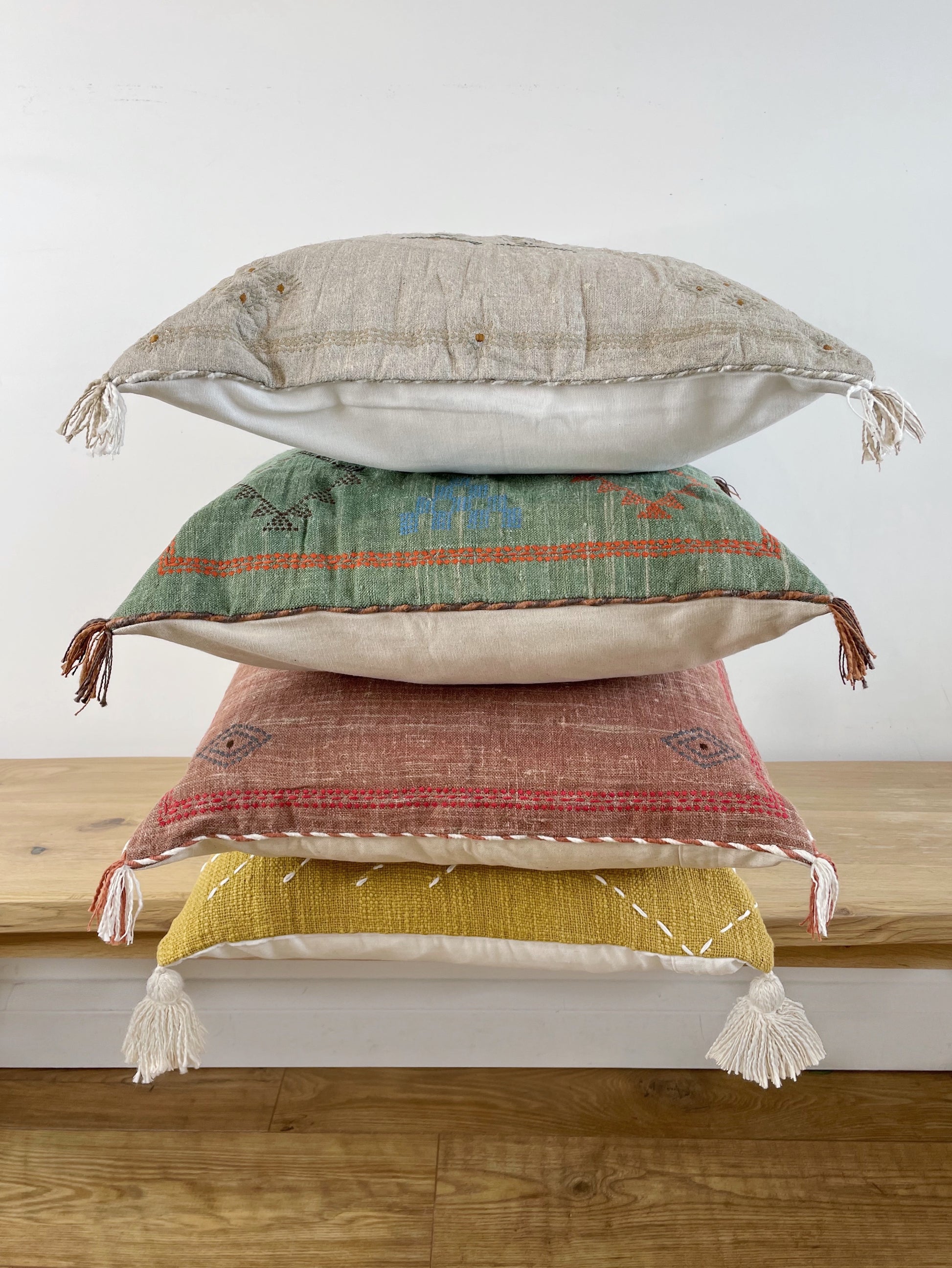 four colourful cushions in a pile, on a bench