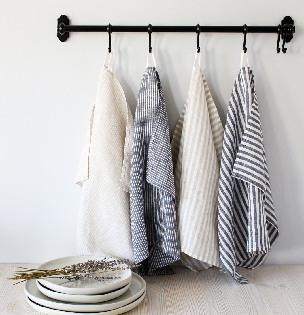 four striped linen tea towels hanging on a black rail