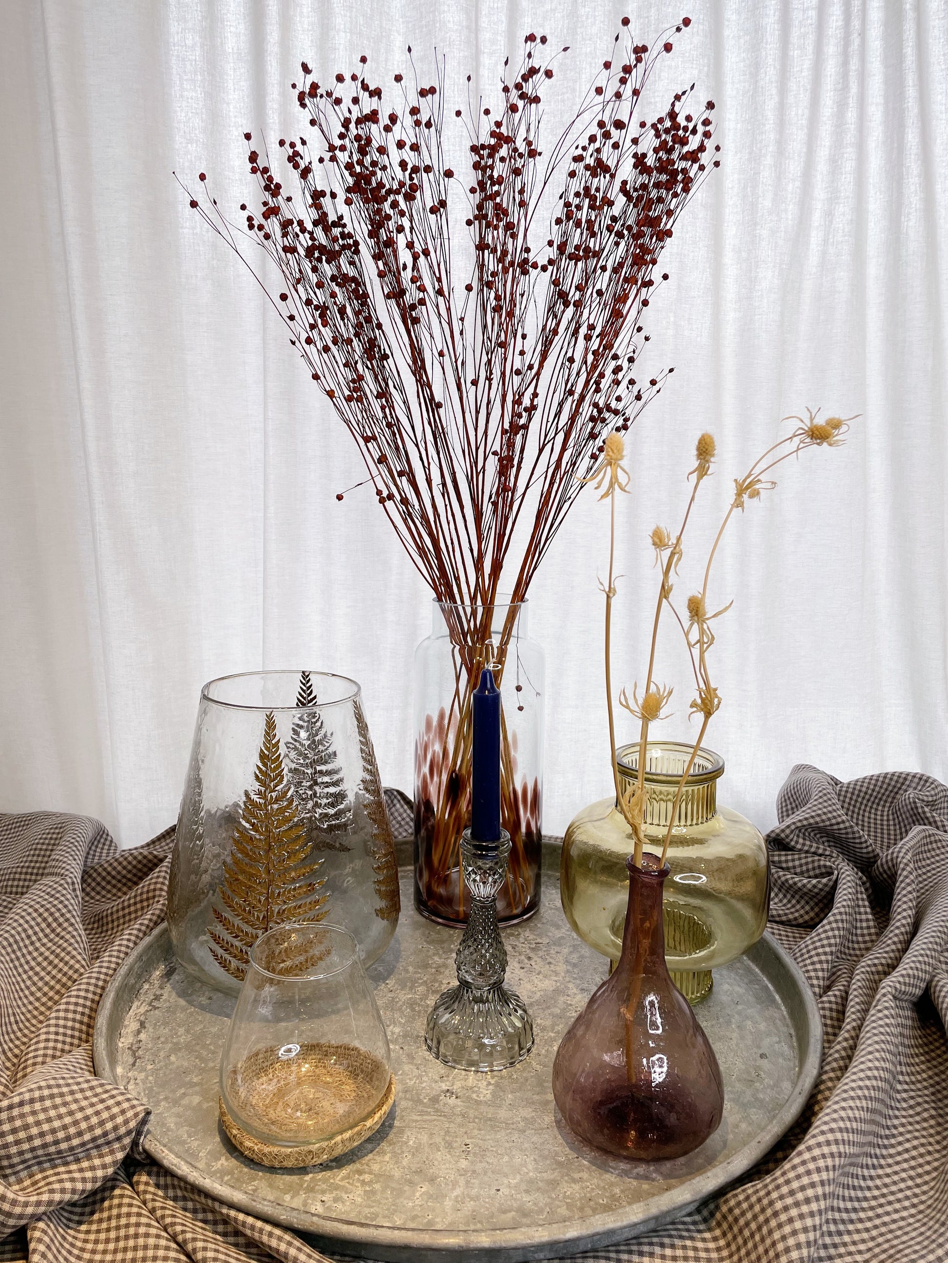 A selection of glass vases and candlesticks/votives on a metal tray, on top of a check table cloth