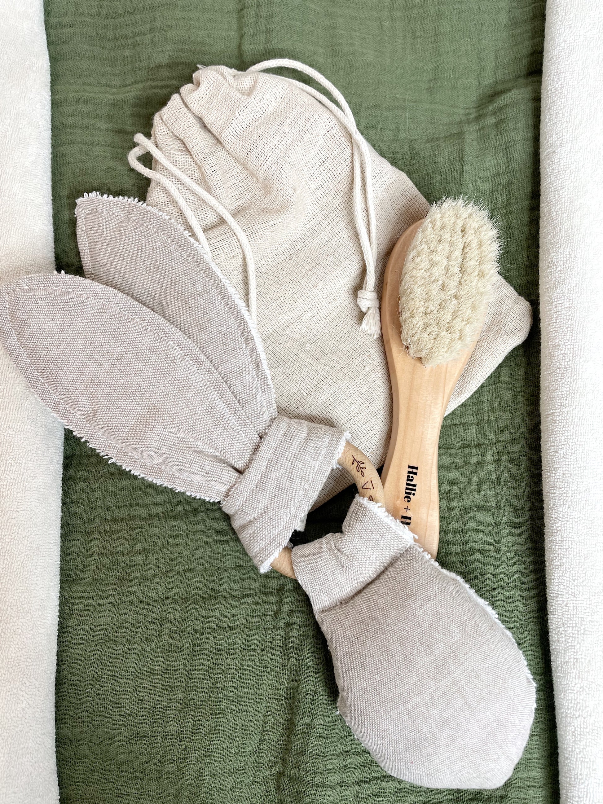 olive green blanket with a soft bristled baby brush and a greige rabbit rattle teether on top