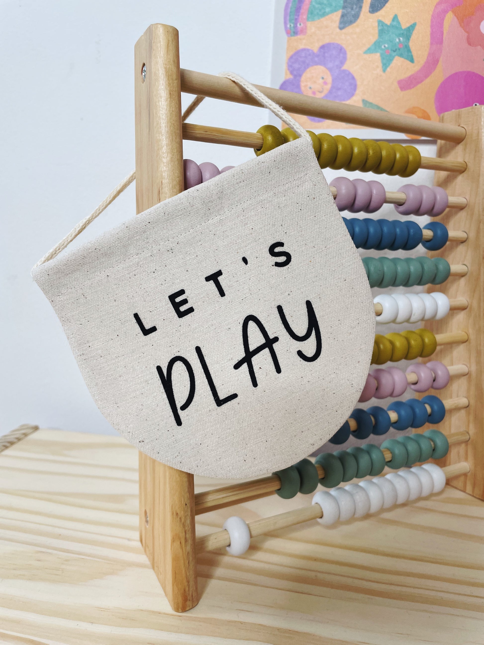 Colourful abacus with a beige banner hanging off it, reading 'Let's Play'