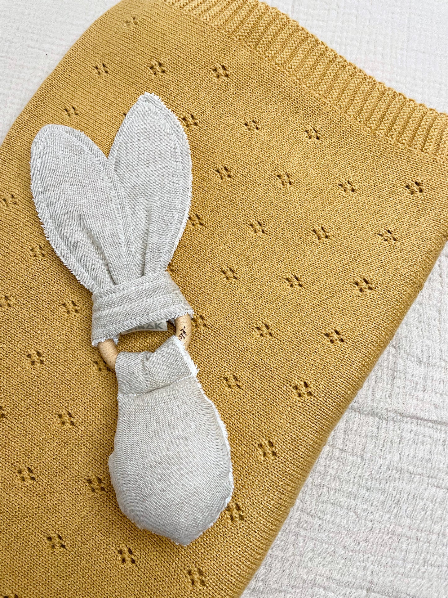 organic cotton blanket in ochre with a greige rabbit teether on top of it 