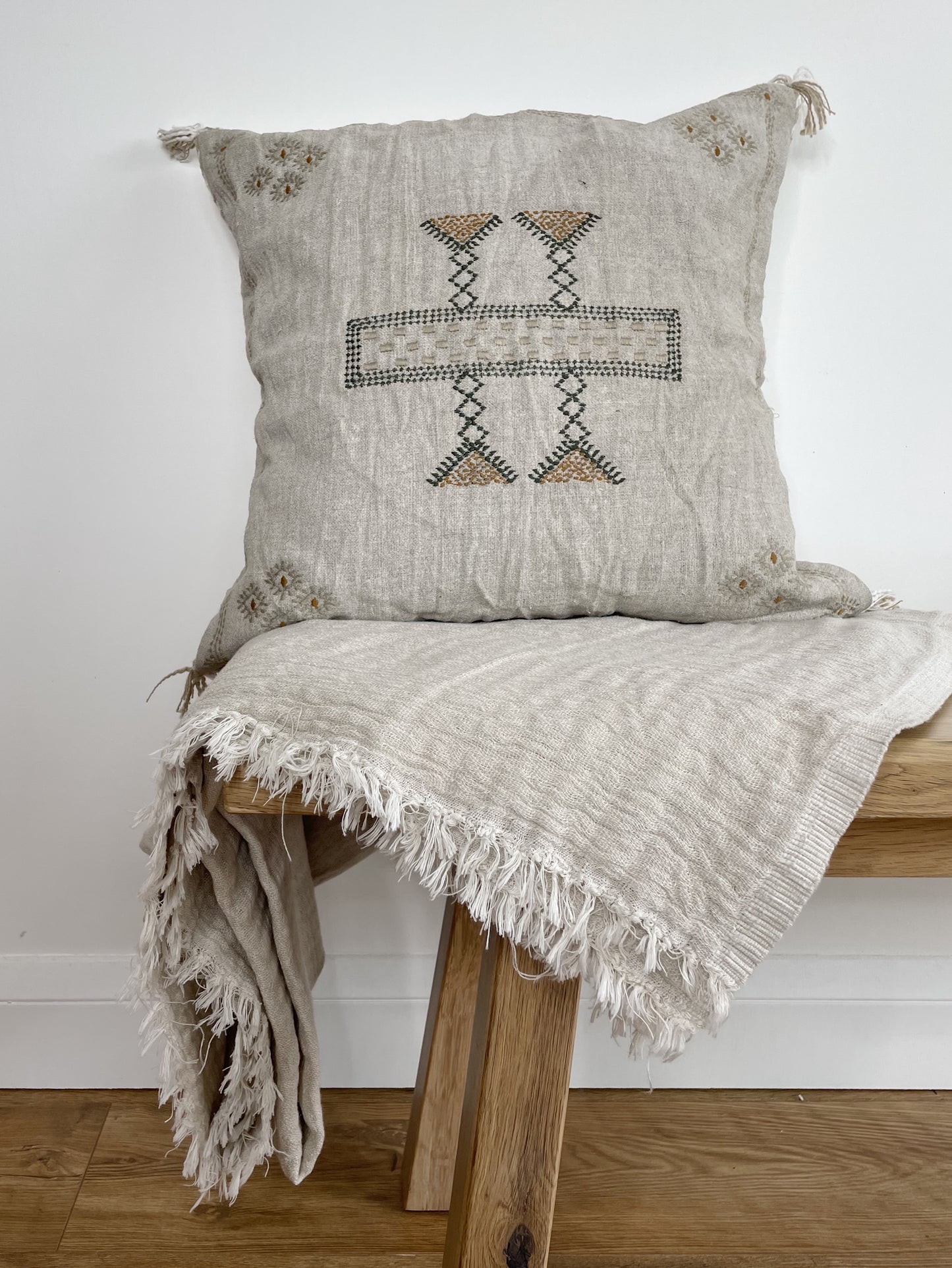 neutral, embroidered cushion on top of a blanket in the same colour, both on a bench