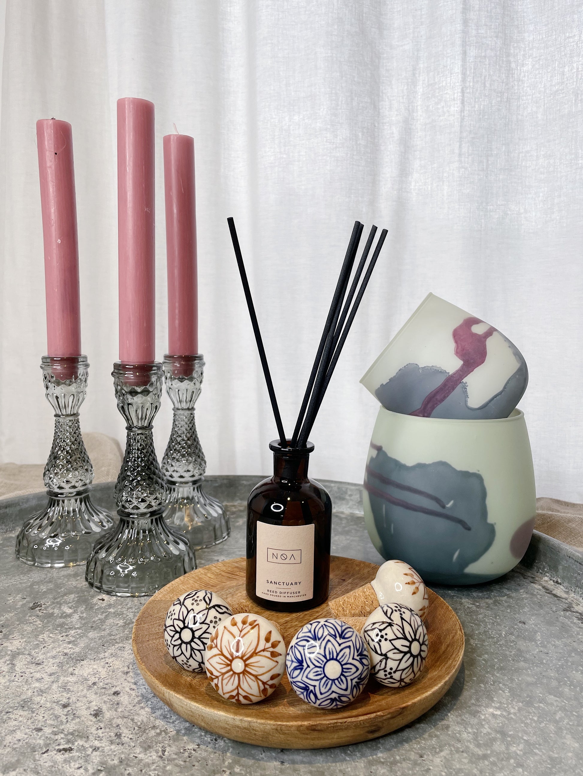 A selection of candlesticks, votives, ceramic bottle stoppers, a diffuser and a wooden plate all on top of a large metal tray