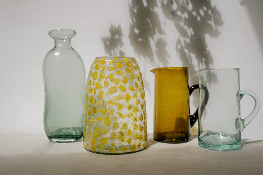 two vases and two jugs on a table with the shadow of some leaves behind them