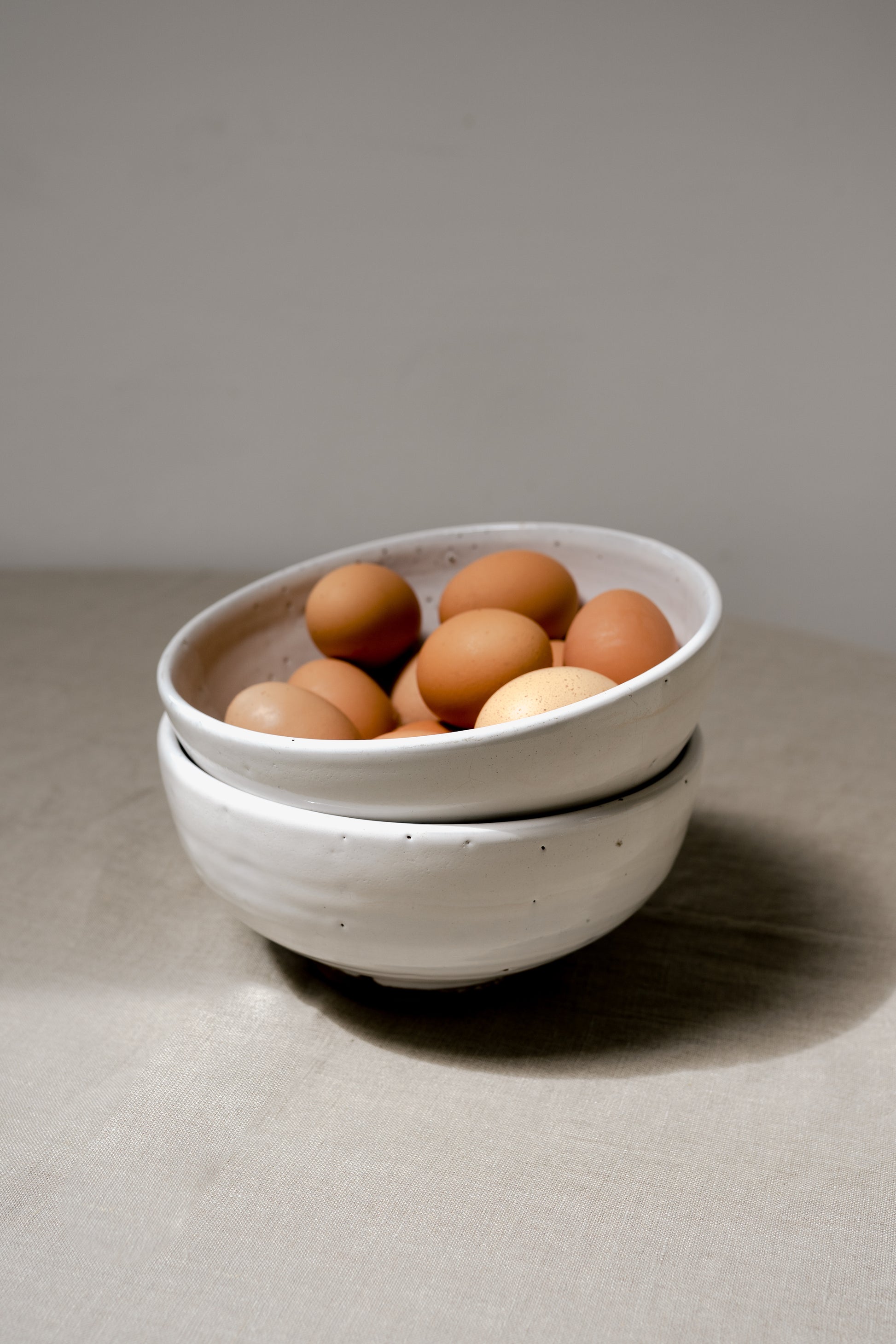 two handmade earthenware white bowls in a pile with eggs in