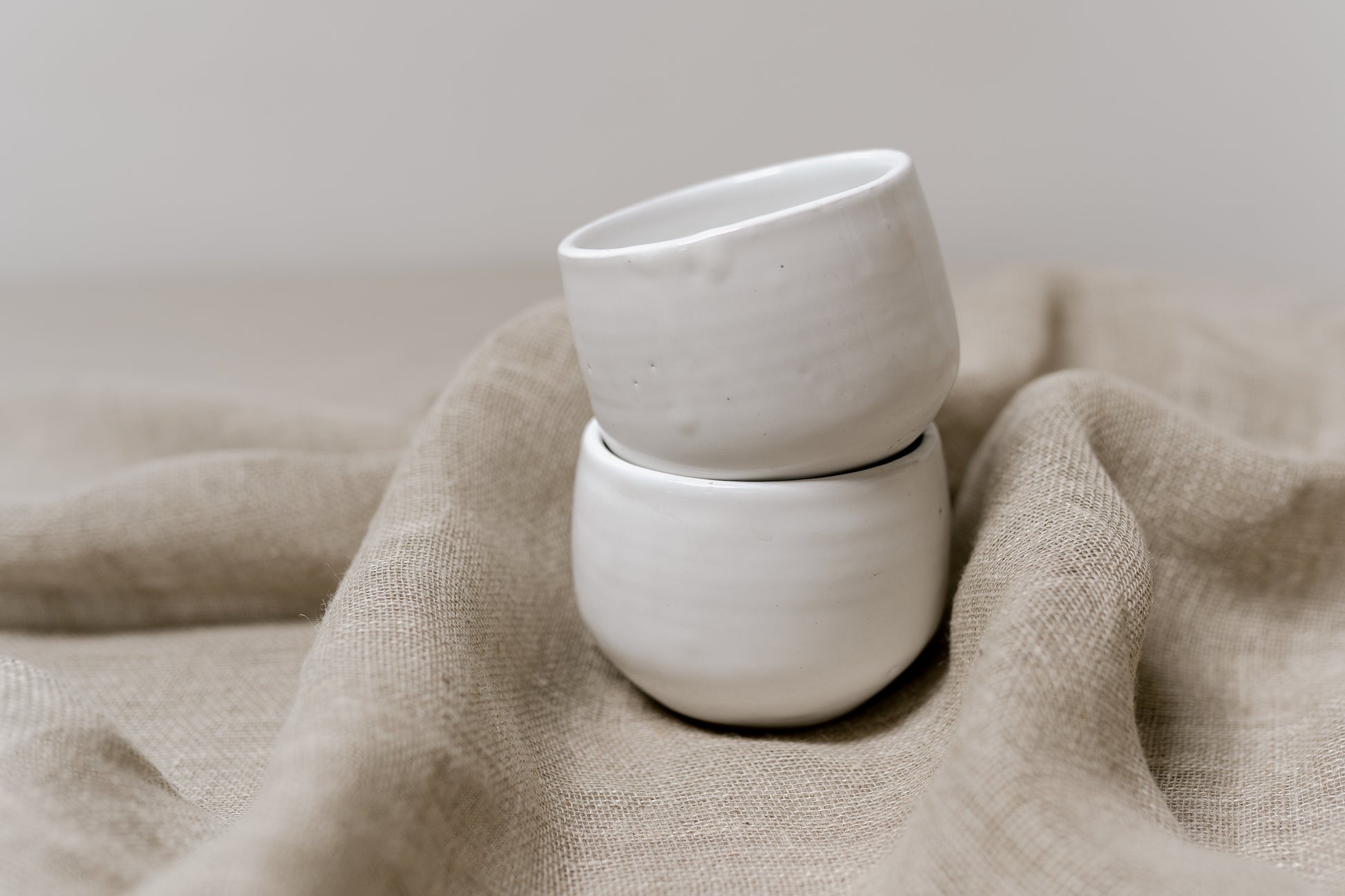 two small white bowls stacked on top of a linen cloth
