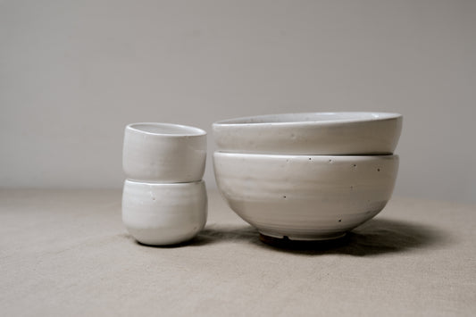two small white bowls and two large white bowls stacked next to each other on top of a linen cloth