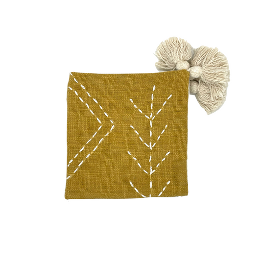 folded yellow cotton cushion cover with white embroidery and tassels
