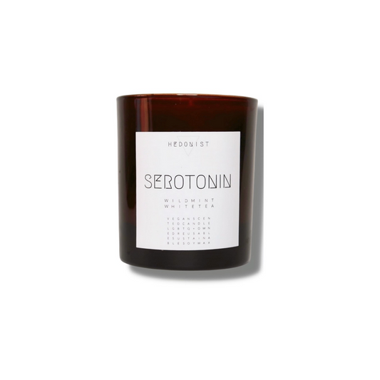 candle in a brown glass jar, with a white label and simple font with the name Serotonin in caps