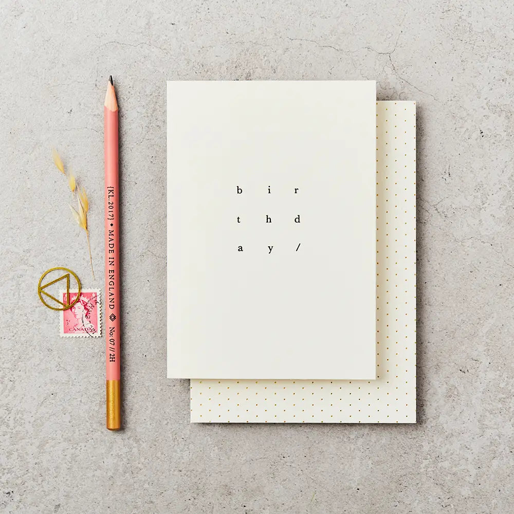 cream greeting card with birthday written on it in simple black type, next to a  pencil and stamp