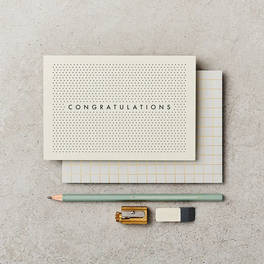 cream greeting card with black text saying 'congratulations', surrounded by polka dots, next to a pencil, sharpener and rubber