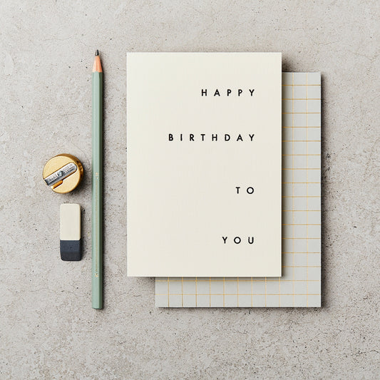 cream greeting card with happy birthday to you in black type, centered to the right. Next to the card is a green pencil, a sharpener and a rubber