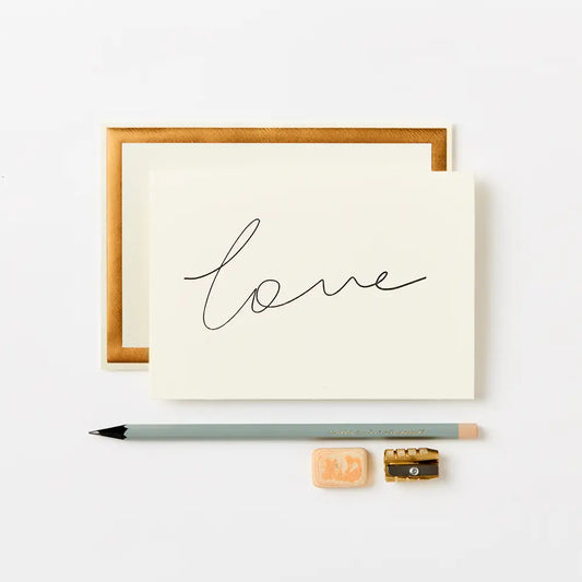 cream greeting card with love written on in black ink, placed next to a green pencil, a sharpener and a rubber