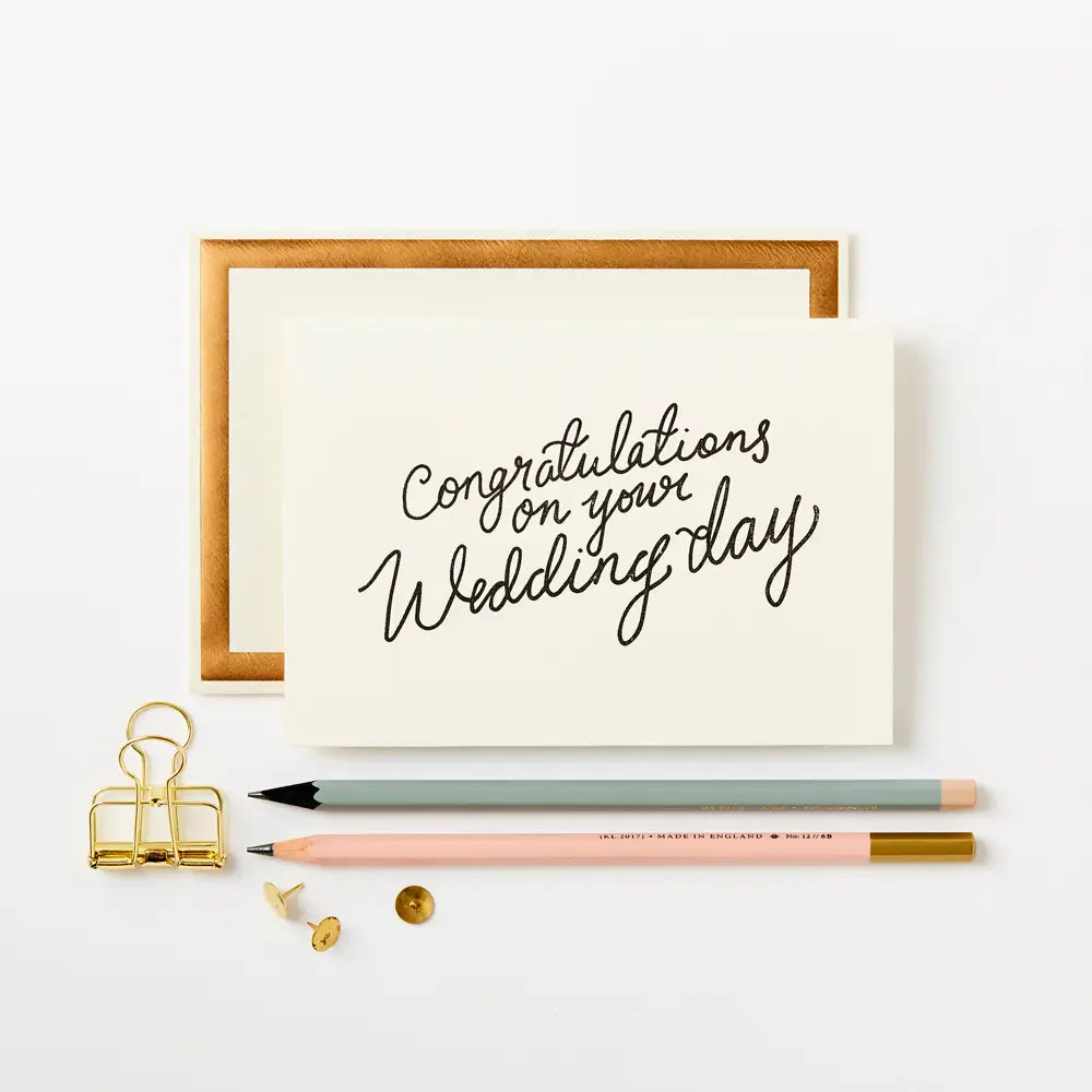 congratulations on your wedding day greeting card next to two pencils and some pins