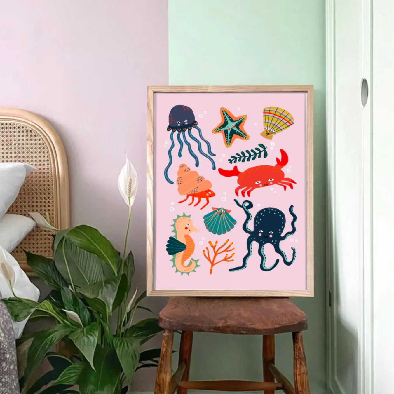 children's print with colourful characters including a crab, seahorse, octopus starfish and much more, sitting on a wooden chair, against a mint green wall and next to a plant