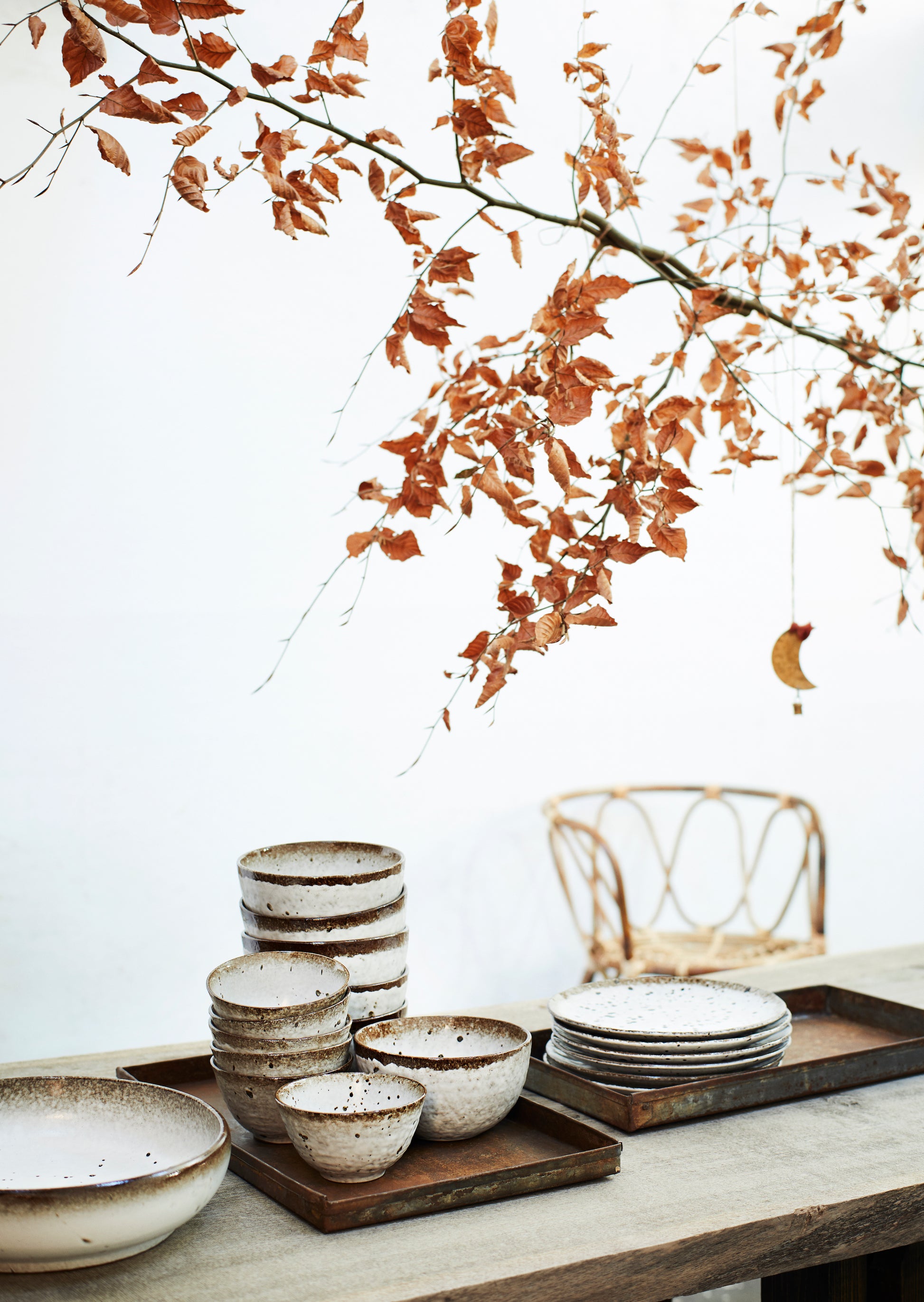 a pile of white and brown stoneware bowls and plates on wooden trays, under a tree with auburn leaves