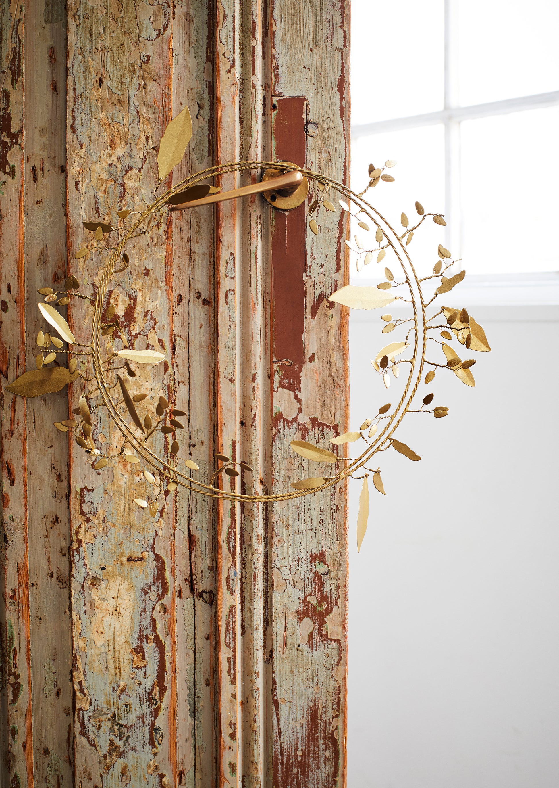 iron wreath hanging on a gold door handle, against a distressed wooden door