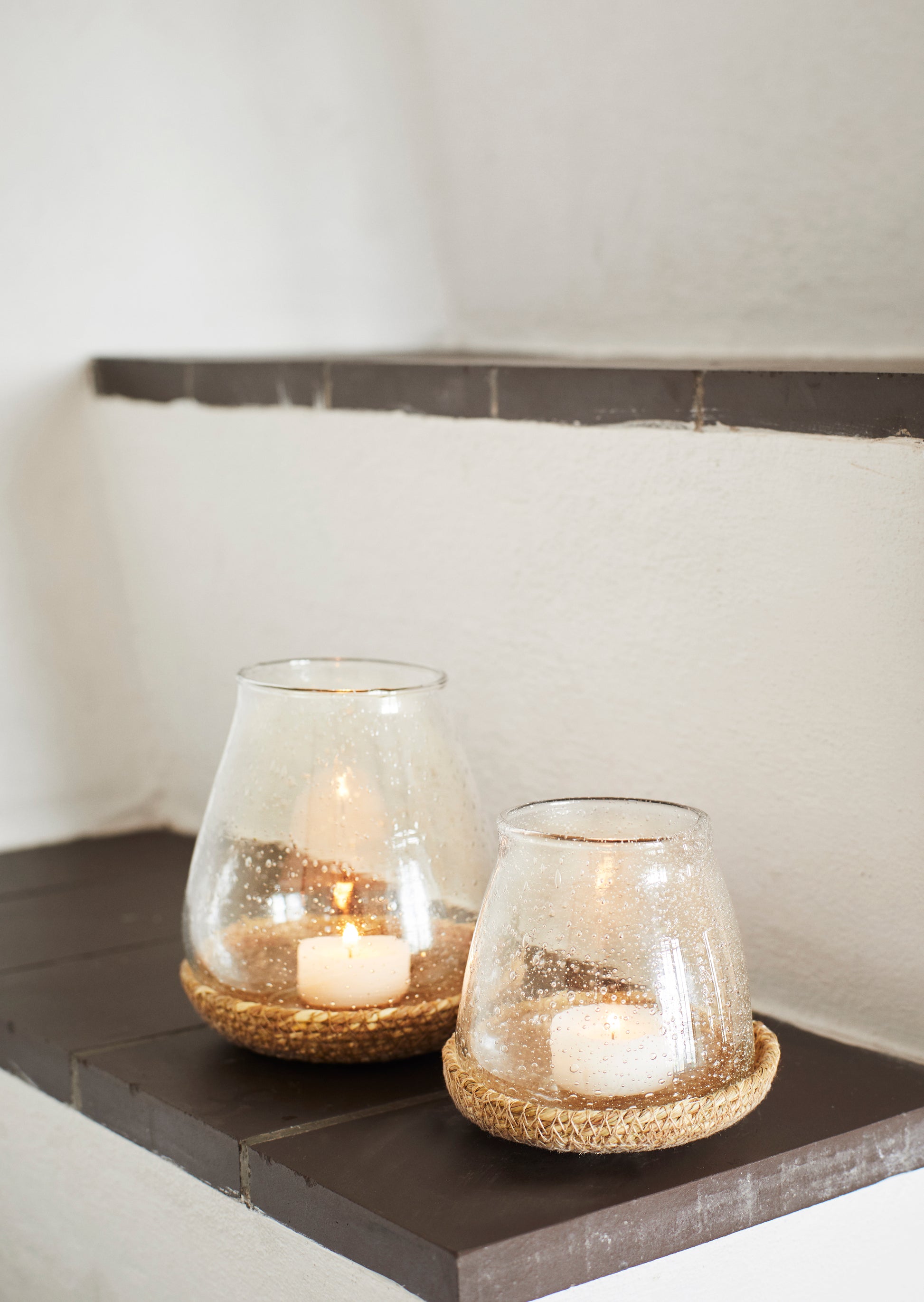 two glass votives, on top of individual jute trays, on a dark brown step