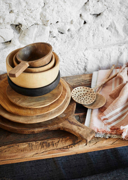stack of wooden plates, servers and bowls on top of a wooden bench, with wooden salad servers and orange/red tea towels